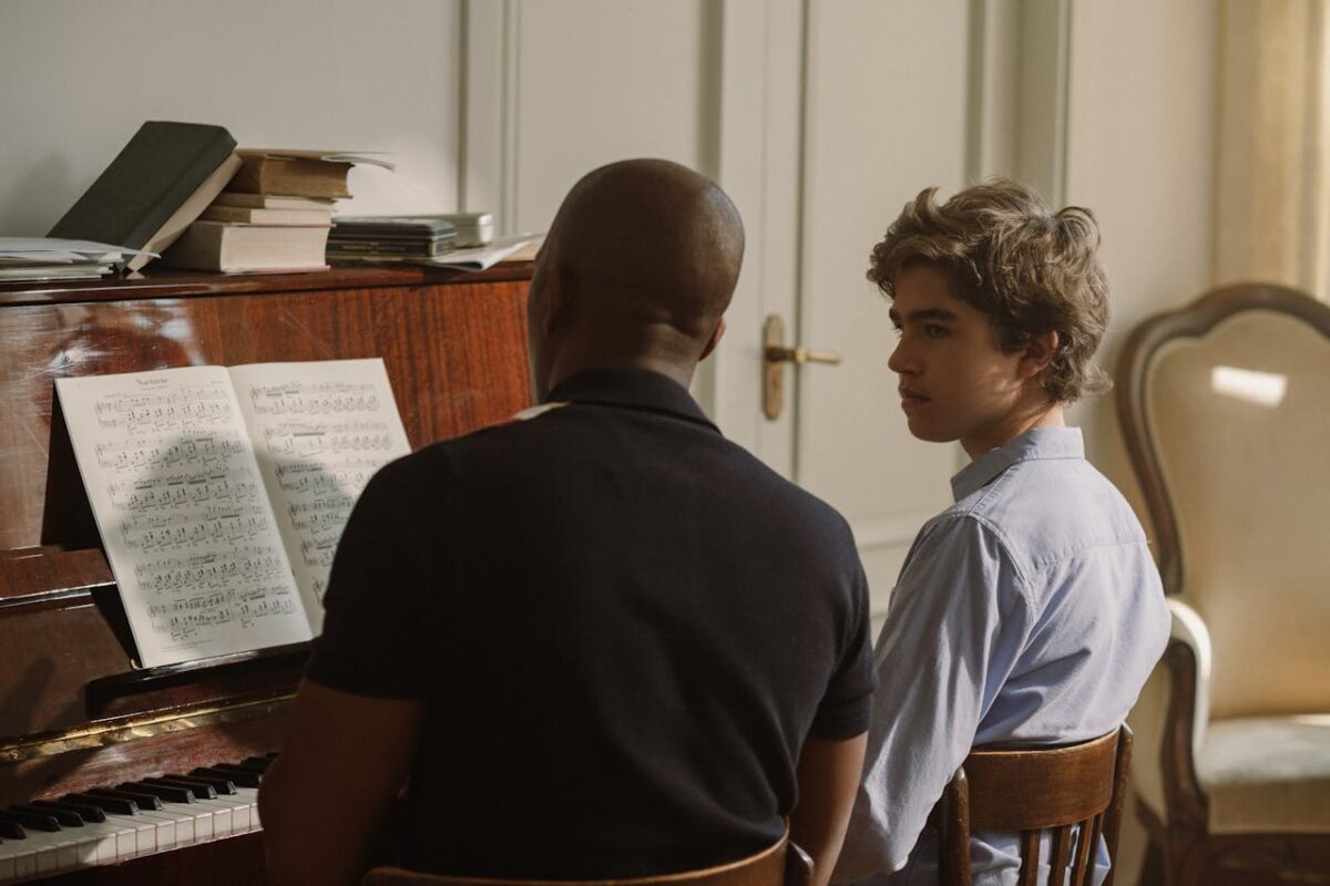 A music teacher guides a student during a piano lesson in a warmly lit room.